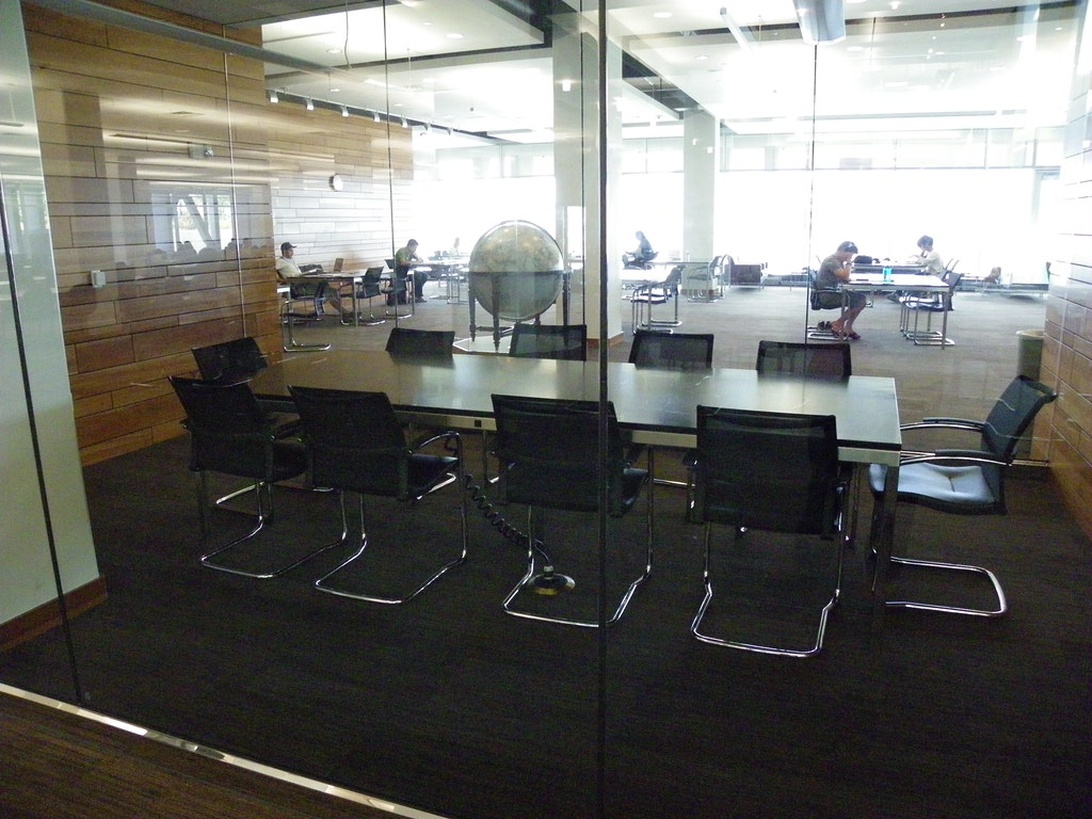 En modern coworking-miljö som visar ett inglasat konferensrum och ett öppet kontorslandskap där flera personer arbetar fokuserat.